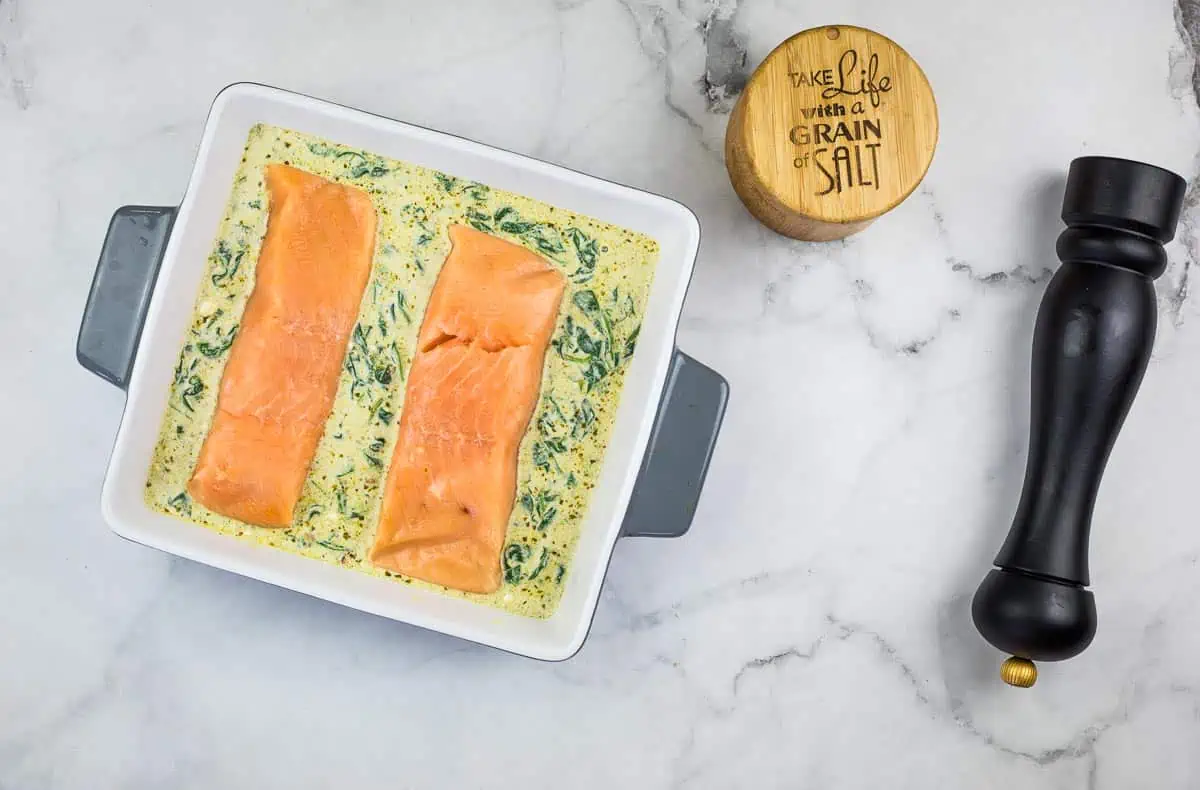 Salmon filets on top of sauce in a casserole dish.