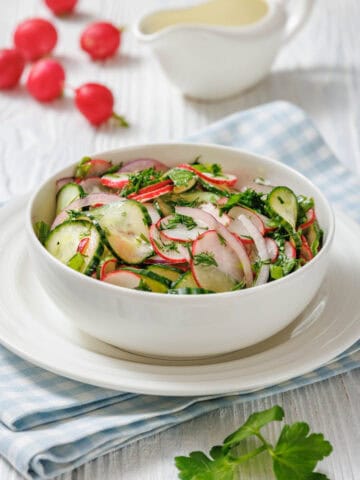 A bowl of radish salad featuring fresh radishes, cucumbers, and parsley, arranged attractively.