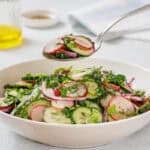 A spoonful of Radish Salad is held above a white bowl filled with the same salad.