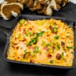 Hot Reuben Dip with chopped dill pickles and herbs in a square skillet served on a slate board with sliced brown bread.