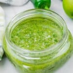 A glass jar filled with freshly blended lime-garlic cilantro marinade, featuring a bright green color and slightly textured consistency.