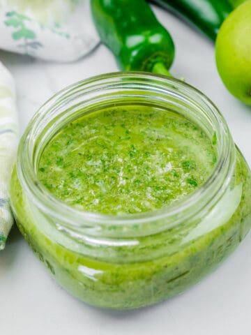 A glass jar filled with freshly blended lime-garlic cilantro marinade, featuring a bright green color and slightly textured consistency.