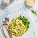 A white plate with egg salad, garnished with greens, is shown with forks, salt and pepper shakers, and a small bowl of sauce.