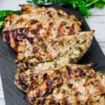 Grilled chicken on a black stone-like board with cilantro leaves in the background.