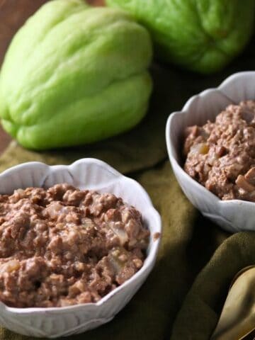 Two cups of Apple Cinnamon Oatmeal with two whole chayote squash and a gold spoon nearby on a wooden surface.