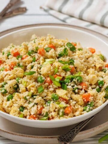 A plate of Cauliflower Fried Rice beside a fork and table napkin.