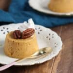 A small white plate with a pumpkin custard topped with pecans and whipped cream.