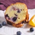 A slice of Blueberry Bundt cake with blueberries and a lemon wedge on a plate.