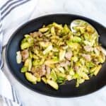 A black plate with Italian Brussels Sprouts with Sausage.