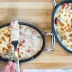 Two skillet pans of Philly Cheesesteak Casserole, one hand holding a fork from the skillet.